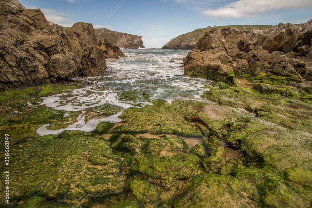 Asturien in Nordspanien: Küstenlandschaft mit weißen Wellen und algenbewachsenen Steinen nahe des Küstenortes Llanes 
