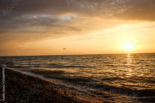 Golden  Fiery sunset on the Black Sea  on the beach. Coast  stones  waves  sun  beautiful sky  clouds. August  Batumi  Georgia. Water  ease  game. plane in the sky  tourism