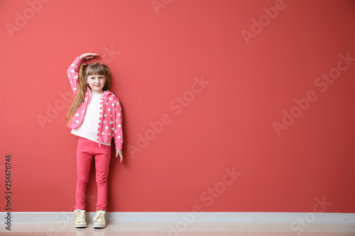 Cute little girl measuring height near color wall