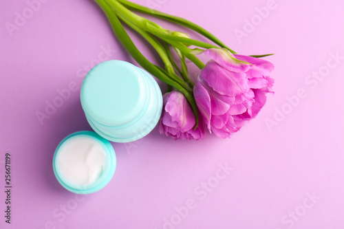 Jars of natural cream with tulips on color background