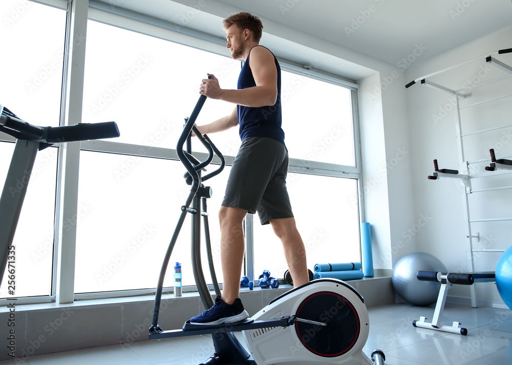 Fototapeta premium Sporty young man training on machine in gym