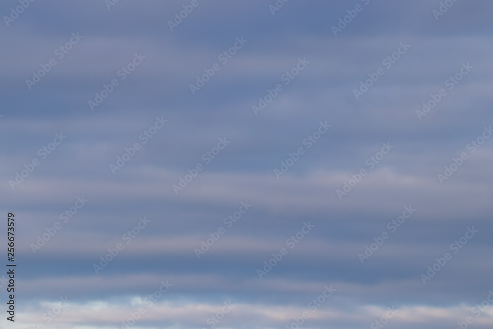 Spring evening sky background with white and grey layered clouds on warm sunset