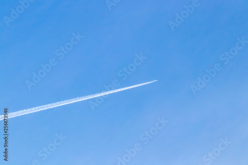 White airplane in blue clear sky leaving white diagonal trace