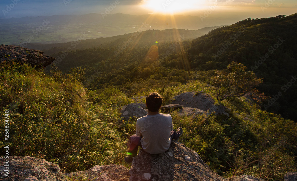 Man sits on a rock and looking at sunset.