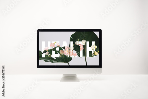 computer with health lettering and tropical green leaves on monitor on desk on white background