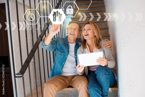 man pointing hand and woman holding digital tablet while sitting on stairs, smart home concept photo