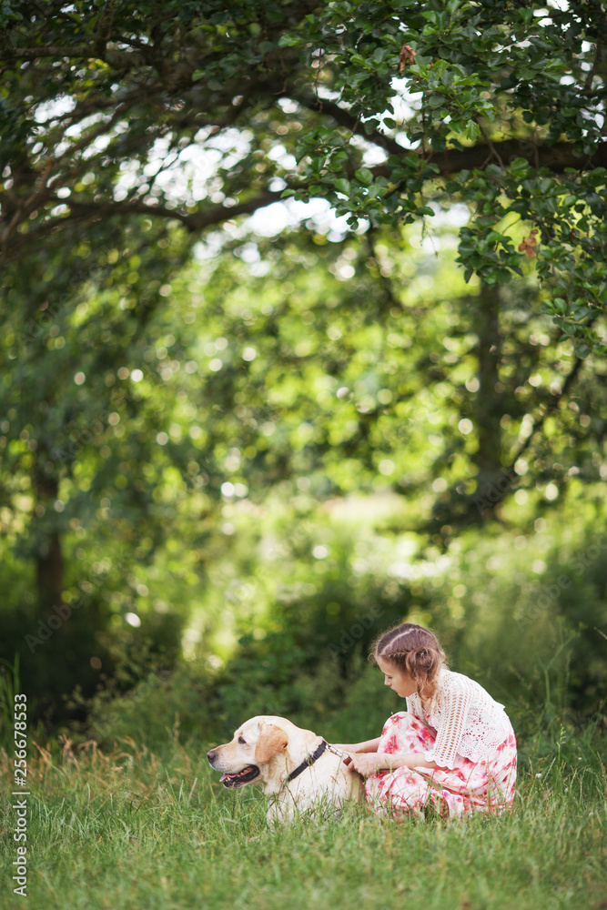 Fototapeta premium Cute smiling little girl hugging and ironing labrador in the summer park