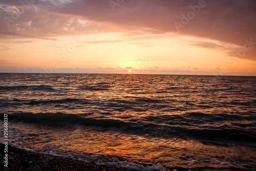 Golden  Fiery sunset on the Black Sea  on the beach. Coast  stones  waves  sun  beautiful sky  clouds. August  Batumi  Georgia. Water  lightness  play. Pink  lilac  crimson