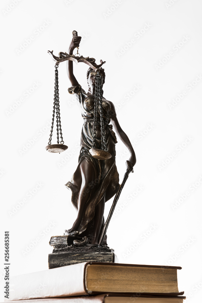 Obraz premium bronze figurine with scales of justice on brown books isolated on white