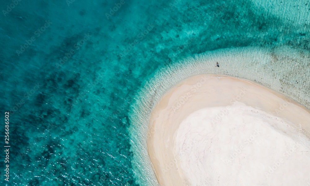aerial view of a female bathing on a tropical desert island beach with crystal turquoise water on vacation in the summer season