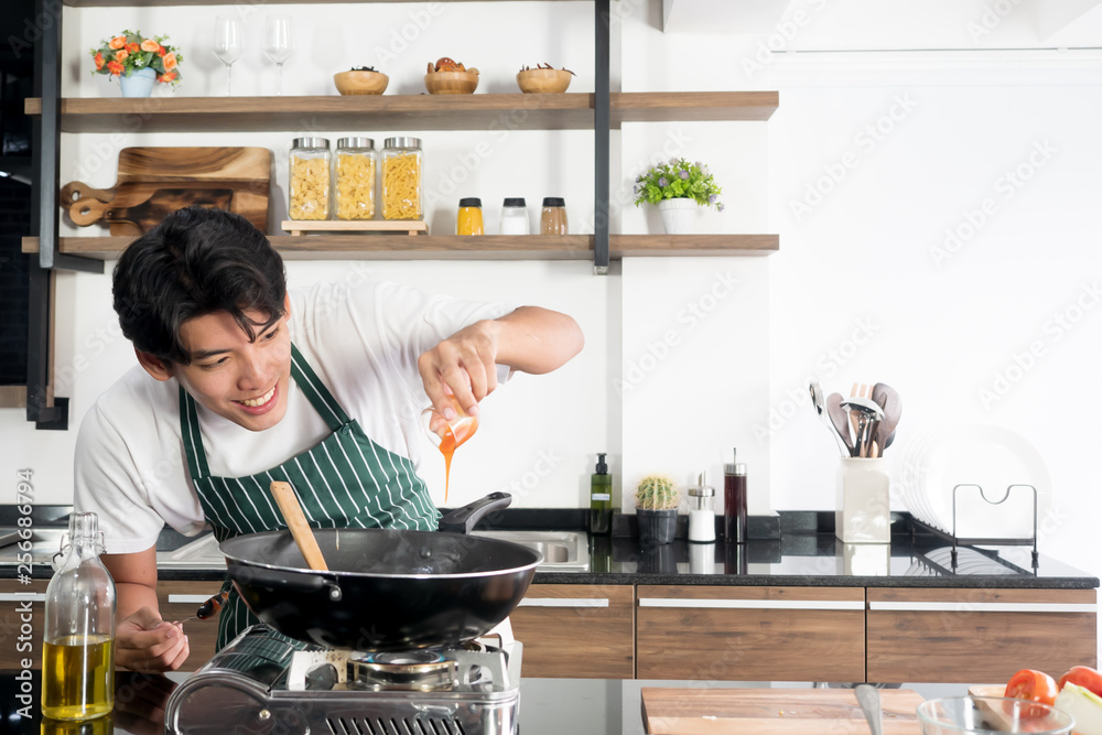 © Manchuya - Young healthy and happy man in apron cooking macaroni in kitchen with smile on face, home cook concept, culinary background © Manchuya - Young healthy and happy man in apron cooking macaroni in kitchen with smile on face, home cook concept, culinary background