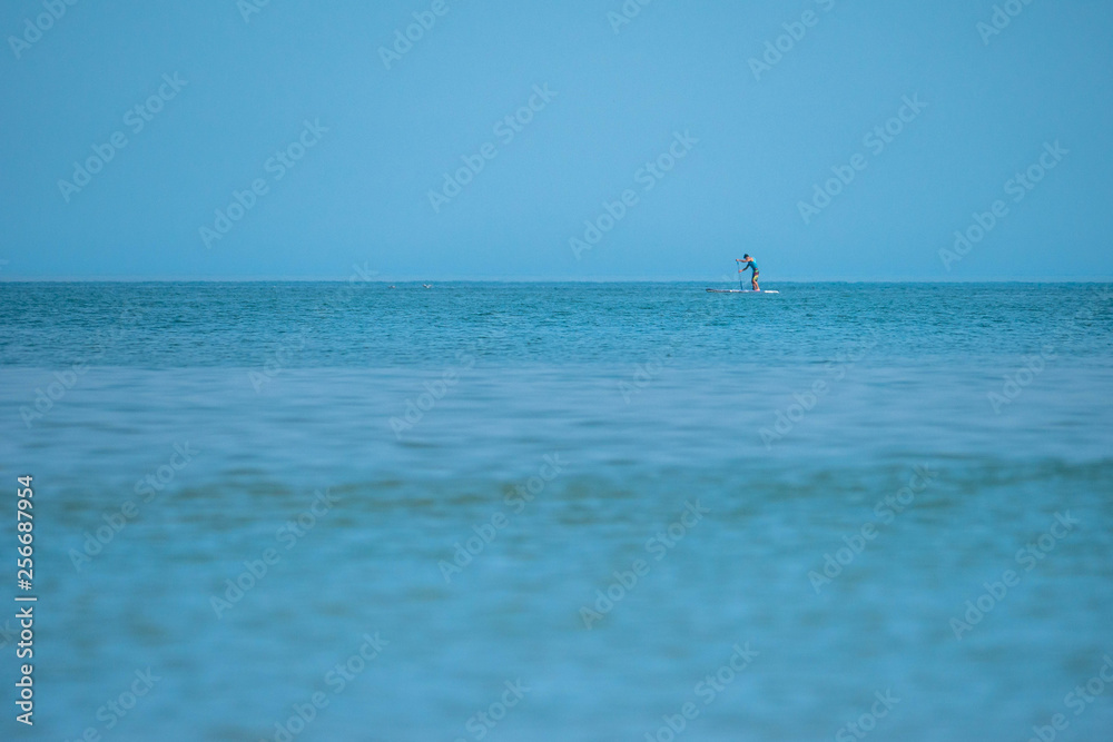 Single male on a stand-up paddle board slightly offshore of a beach in northern France Single male on a stand-up paddle board slightly offshore of a beach in northern France