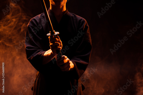 Cropped view of young man in kimono holding kendo sword in smoke