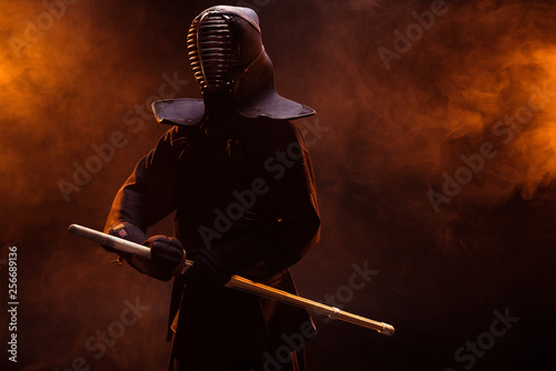 Kendo fighter in armor holding bamboo sword in smoke