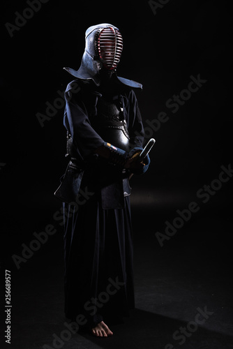 Full length view of kendo fighter in helmet holding bamboo sword on black