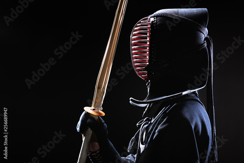 Side view of kendo fighter in traditional helmet holding bamboo sword on black photo