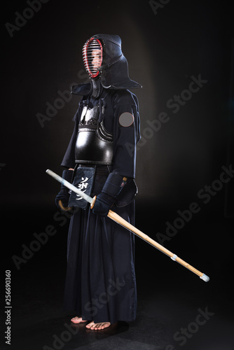 Full length view of kendo fighter in armor holding bamboo sword on black