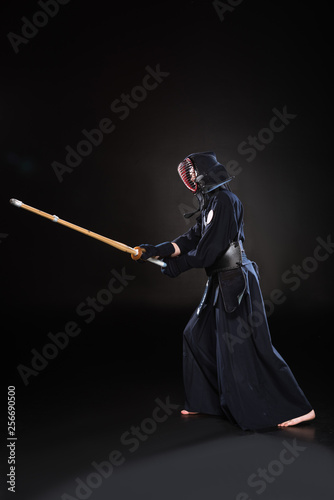 Side view of kendo fighter in armor practicing with bamboo sword on black