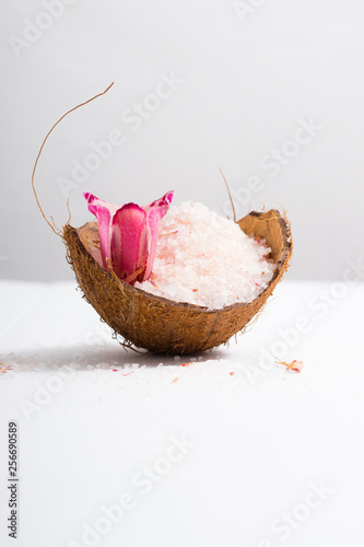 pile of pink bath salt with orchid flower at coconut shell bowl, white wood table