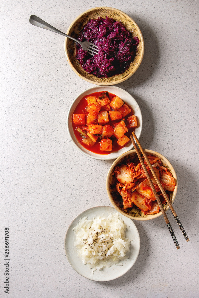Fototapeta premium Variety of fermented food korean traditional kimchi cabbage and radish salad, white and red sauerkraut in ceramic plates with chopsticks and fork over grey spotted background. Flat lay, space