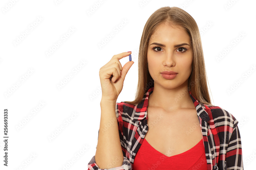 Close up portrait of a beautiful young woman holding a pill looking to the camera seriously isolated copy space. Attractive female patient taking medications. Pharmacy, health, birth control concept Close up portrait of a beautiful young woman holding a pill looking to the camera seriously isolated copy space. Attractive female patient taking medications. Pharmacy, health, birth control concept