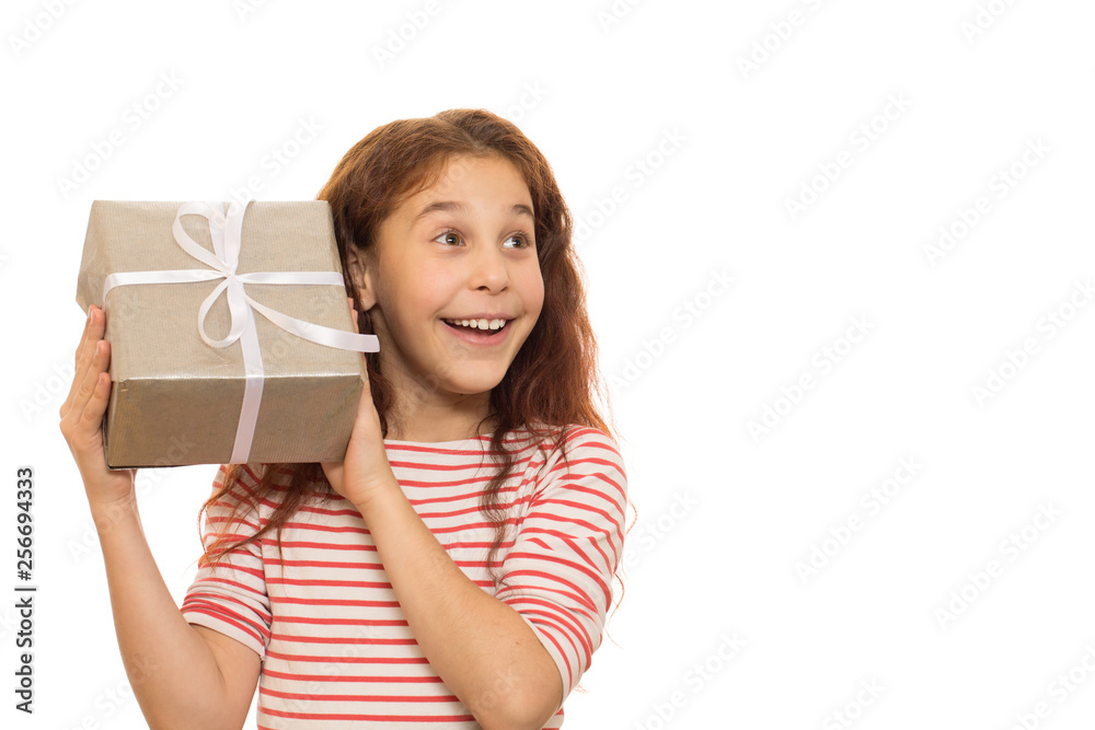 Cute young happy girl holding Christmas present to her ear listening carefully guessing what is in the gift box isolated on white party celebrating holidays surprise wishing Santa Claus x-mas children Cute young happy girl holding Christmas present to her ear listening carefully guessing what is in the gift box isolated on white party celebrating holidays surprise wishing Santa Claus x-mas children