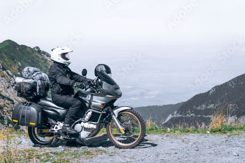 Fototapeta Naklejka Na Ścianę i Meble -  Biker is sitting on his adventure motorcycle, the top mountain in background, enduro, off road, beautiful view, danger road in mountains, freedom, extreme vacation. Transfagarasan Romania