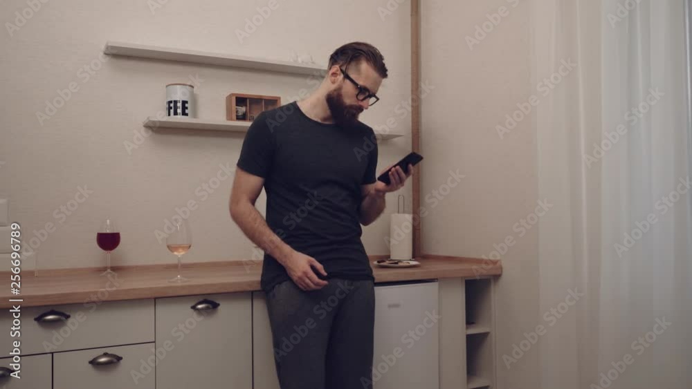 Bearded man with smartphone and glass of wine at kitchen, slow motion Bearded man with smartphone and glass of wine at kitchen, slow motion