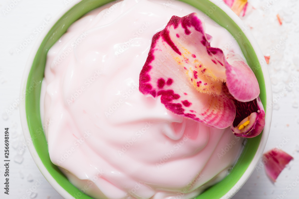 cosmetic cream with pink flower petals, white wood table cosmetic cream with pink flower petals, white wood table