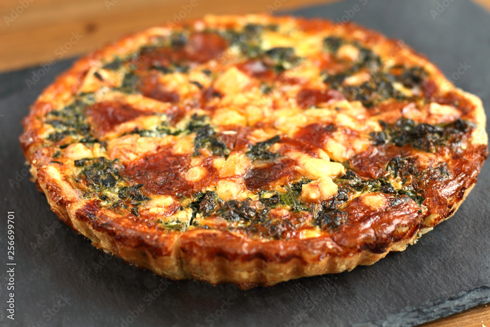 Italian traditional rustic quiche pizza with cheese, spinach  and tomatoes on a black plate in restaurant