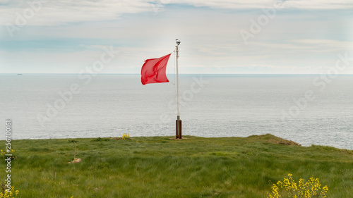 Red flag in the wind, seen on the South West Coast Path near Emmett's Hill, Jurassic Coast, Dorset, UK