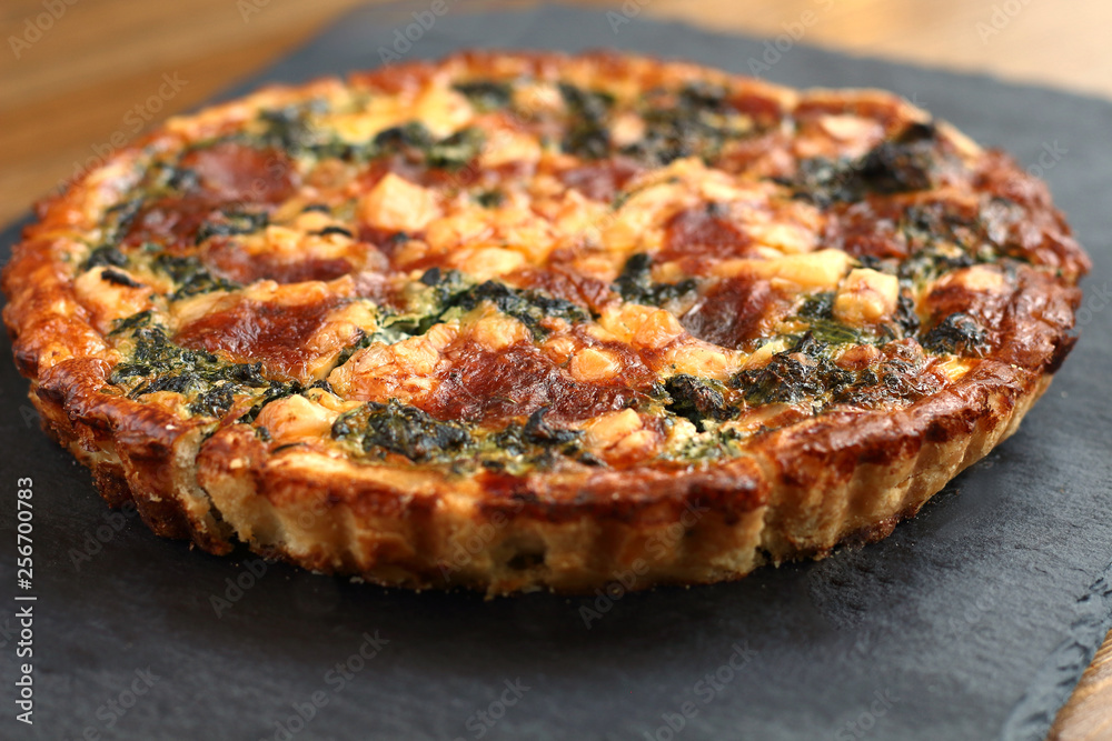 Italian traditional rustic quiche pizza with cheese, spinach  and tomatoes on a black plate in restaurant