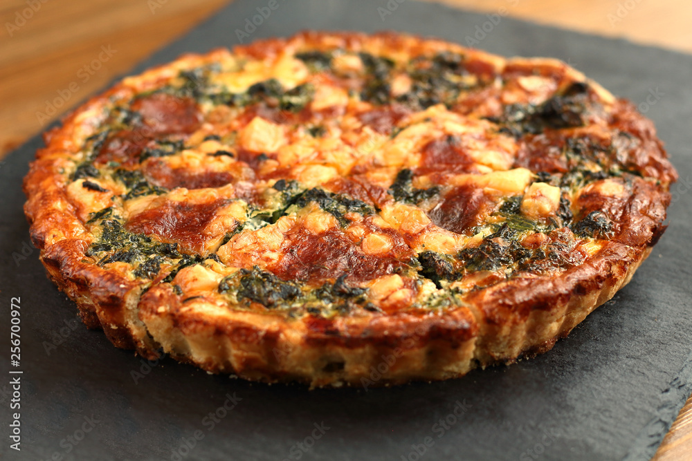 Italian traditional rustic quiche pizza with cheese, spinach  and tomatoes on a black slate plate in restaurant