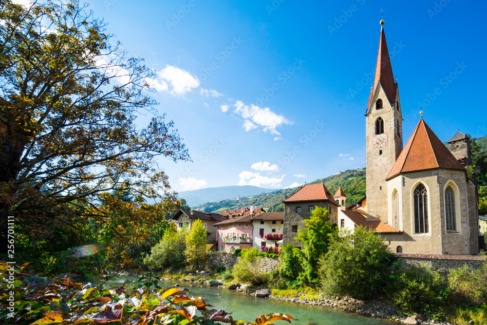 church and colorful houses along river Isarco, Chiusa, Italy