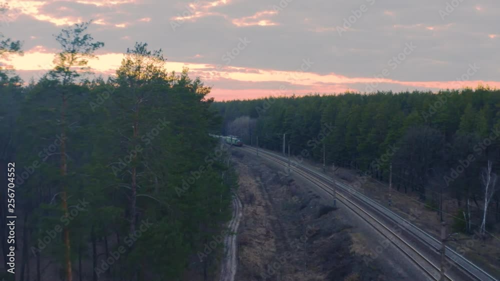 Aerial view of the freight train, carrying rubble and cement, moving on the spring forest at sunset Aerial view of the freight train, carrying rubble and cement, moving on the spring forest at sunset