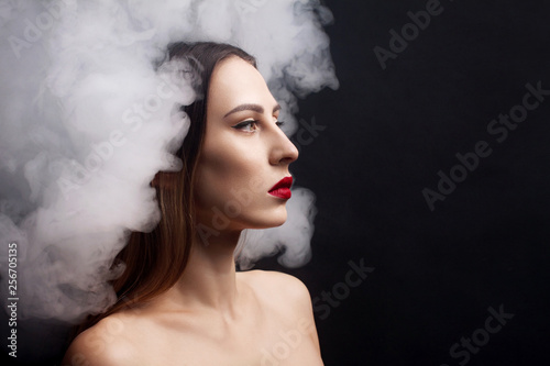 Attractive young girl and white smoke. Black background.