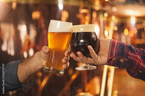 Photos Cropped close up of two men clinking beer glasses together, celebrating at the beer pub