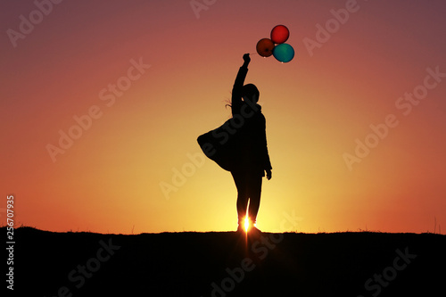 The girl with colorful balloons on the background of the sunset