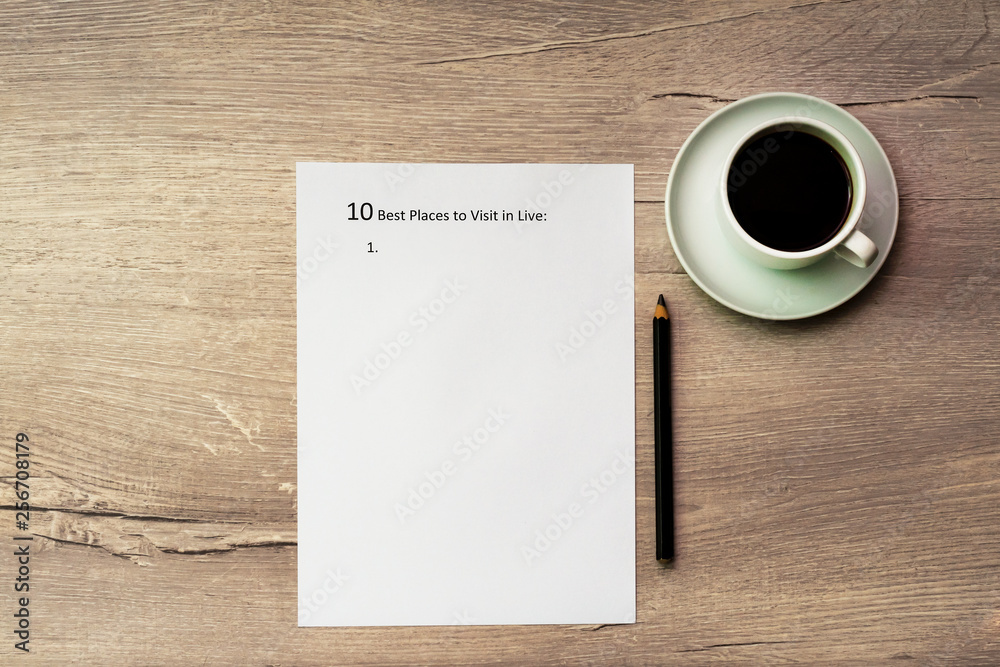 The inscription on a white sheet of A4: 10 best plases to visit in live. On a wooden background, сup of coffee.