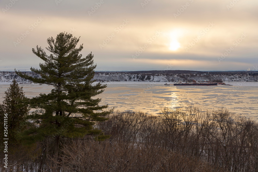 Horizontal bird’s eye view from the Plains of Abraham of the partly frozen St. Lawrence river in winter with merchant boat moored on its south shore, Quebec City, Quebec, Canada