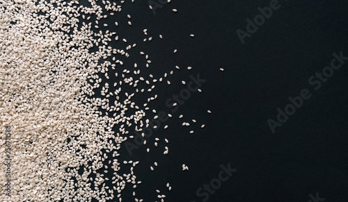 Scattered white sesame seeds on black textured paper background. Calcium concept. Close up, copy space, top view.