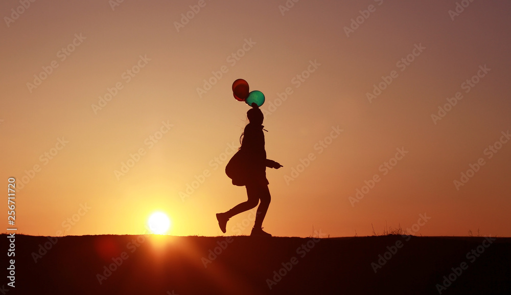 Girl runs with balloons on the background of the sunset to the sun