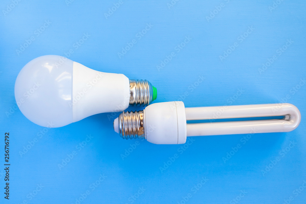 LED and energy-saving light bulbs lie side by side on a blue background LED and energy-saving light bulbs lie side by side on a blue background
