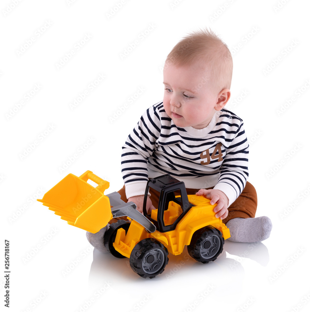 Pretty baby boy plays with toy, isolated on white background with shadow reflection. Adorable small boy playing with plastic yellow excavator toy. Toddler sits next to an excavator, studio shot. Pretty baby boy plays with toy, isolated on white background with shadow reflection. Adorable small boy playing with plastic yellow excavator toy. Toddler sits next to an excavator, studio shot.