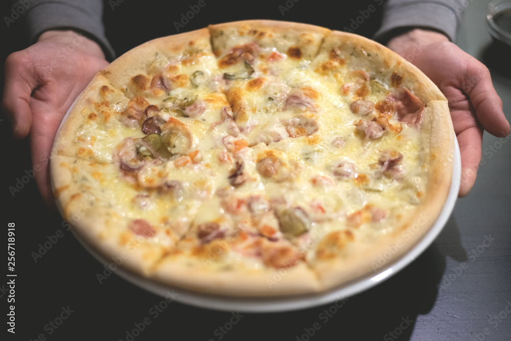 Fresh pizza on the plate in the hands on a wooden table background.