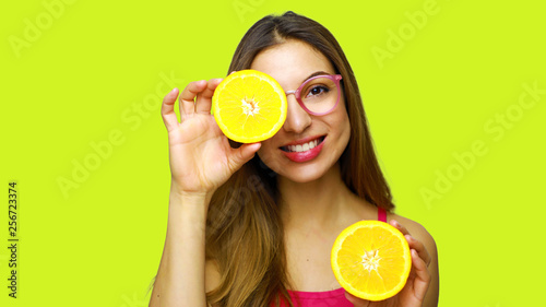 Smiling girl with glasses hiding eye behind half orange with yellow background