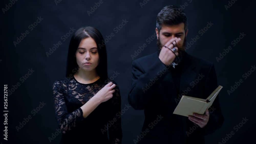 Girl and priest dressed in black baptized on a black background. Priest prays on a black background. Religious nun in religion concept against dark background. religion opium for the people. Girl and priest dressed in black baptized on a black background. Priest prays on a black background. Religious nun in religion concept against dark background. religion opium for the people.