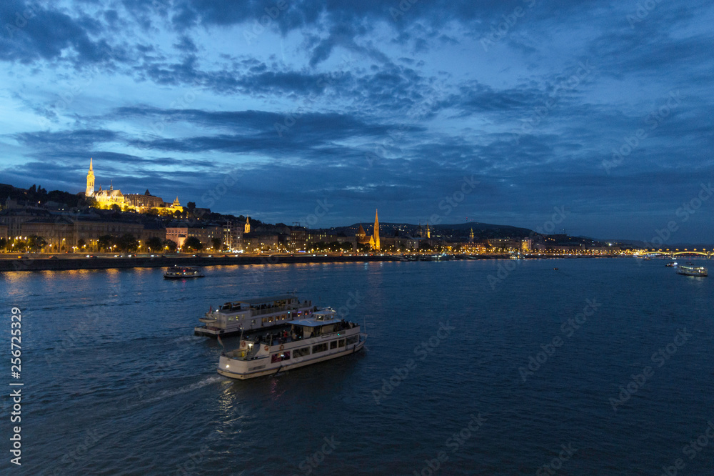 Two ships move away on the Danube as it passes through Budapest with Fishermen's Bastion and the illuminated Buda shore, Hungary