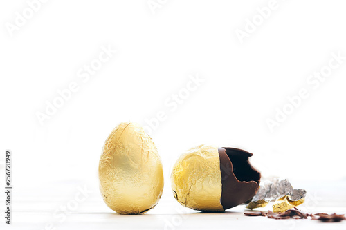 Wall Mural Stylish Easter egg in golden foil and broken chocolate egg with chocolate pieces in white light with space for text