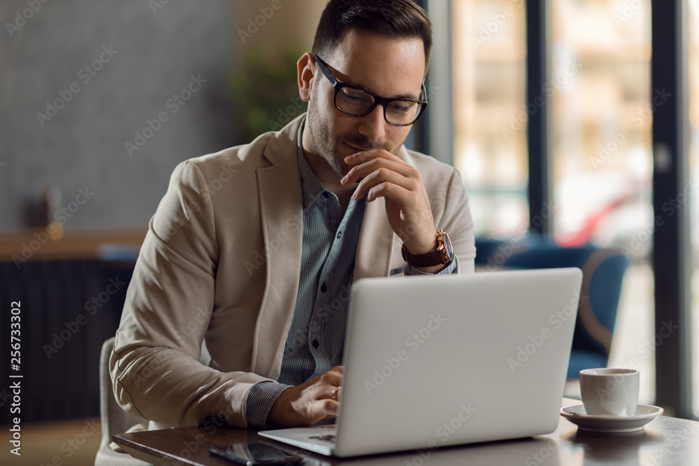 Serious businessman reading an e-mail on a computer while having coffee break in a cafe Serious businessman reading an e-mail on a computer while having coffee break in a cafe